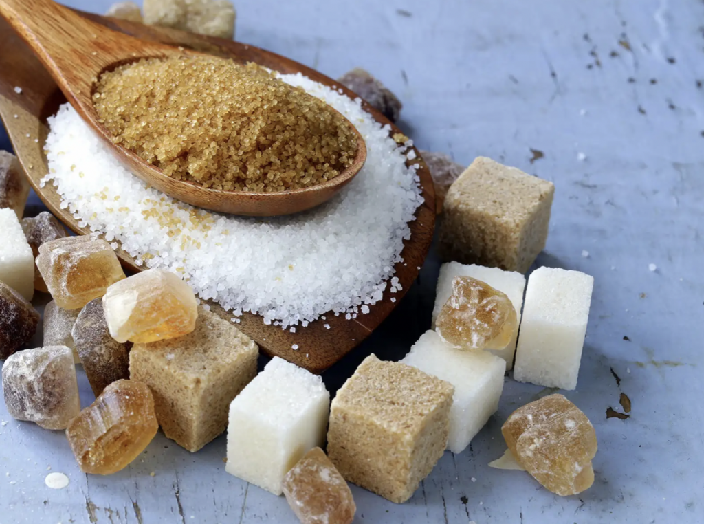 Grains and cubes of white and brown sugar on a wooden table.
